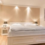 Bedroom with white bed, nightstands, and wardrobe. Wall lighting and picture on the wall.