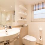 Bathroom with sink, toilet, and window with roller blind.