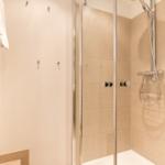 Shower with glass enclosure and handheld shower, next to towel warmer.