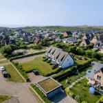Aerial view of a residential area with houses, gardens, and a distant coastline.