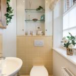 Badezimmer mit Waschbecken, Toilette und Fenster mit Blumen.