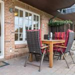 Terrasse mit Holztisch, Stühlen und Sitzgelegenheit. Hinterhof mit Steinmauer und Holzzaun.