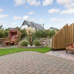 Garten mit Terrasse, Liege, Tisch und Stühle, Holzzaun und Grünflächen.