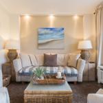Wohnzimmer mit Sofa, Tisch und Wandbild. Fenster mit Vorhängen.