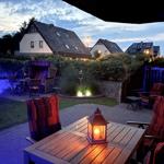 Terrasse mit Tisch, Stühlen und Laterne. Hinterhof mit Garten, Beleuchtung und Haus im Hintergrund.