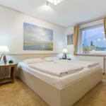 Schlafzimmer mit Doppelbett, Fenster mit Leuchtturmansicht und Wicker-Sofa.