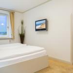 Schlafzimmer mit Bett, TV und Fenster mit Blick auf Leuchtturm.
