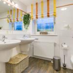 Badezimmer mit zwei Waschbecken, Toilette und Fenster mit Meerblick.