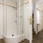 Dusche mit Glaswand und Duschbrause im Bad. Flur mit Treppe und Tür.