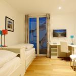 Room with two beds, desk and TV. Windows with curtains.