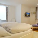 Bedroom with double bed, TV, and chair. Windows with curtains and wall art.