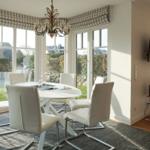 Dining area with round table and white chairs. Large windows overlooking the garden.