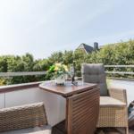 Terrace with table, chairs, and flower arrangement. View of green hedge and roof.