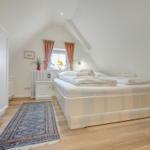 Bedroom with double bed, wooden floor, and window with curtains.