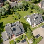 Aerial view of several houses with green gardens and parked cars.