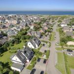 Aerial view of a coastal village with houses, greenery, and the sea in the background.
