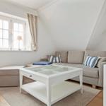 Living room with sofa, glass table, and windows. Attic with wooden floor and wall art.
