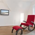A room with red armchair and footstool, wall-mounted TV, and window.