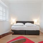 Bedroom with bed, nightstands, and window. Wooden floor and red seat.