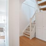 House with staircase and door, view into living room with window and seat.