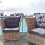 Two wicker chairs with gray cushions on a terrace with a view of houses.