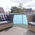 Terrace with rattan sofa and chairs, view of rooftops and trees.