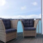 Two chairs with cushions are on the terrace. Background: blue sky and buildings.