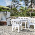 Terrace with white table and chairs and beach chair. Background: stone wall and green areas.