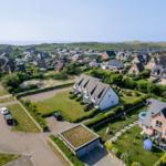 Aerial view of a residential area with houses, green lawns, and distant dunes.