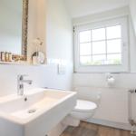 Bathroom with sink, toilet, and window. Mirror with decorative frame.