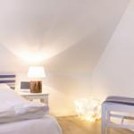 Bedroom with bed, nightstand, lamp, and chair under sloped ceiling.