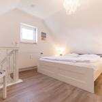 Bedroom with sloped ceiling, white bed, and wooden floor. Window and nightstand visible.