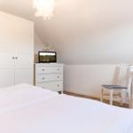 Bedroom with white bed, wardrobe, dresser, and chair under sloped ceiling.