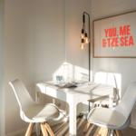 White dining set with chairs and wall art. Dishware in open cabinet.