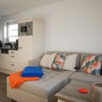 Living room with sofa, cushions, and kitchen area in background.