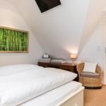Schlafzimmer mit Dachschrägen, Bett, Wickerstuhl und Bad im Hintergrund.