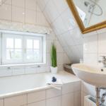 Badezimmer mit Dusche, Waschbecken und Fenster unter Dachschrägen.