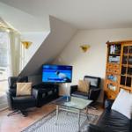 Wohnzimmer mit TV, zwei Sesseln, Sofa und Glasplatte. Fenster zur Terrasse.