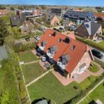 Haus mit rotem Dach, Terrasse und Garten. Umgebung mit weiteren Häusern und Grünflächen.