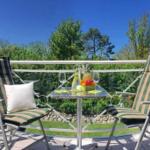 Balcony with two lounge chairs, table, and fruit. Greenery and clear sky in background.