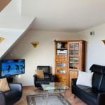 Wohnzimmer mit Sofa, Sessel und Fernseher unter Dachschräge