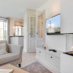 Wohnzimmer mit Sofa, Kamin und Fernseher. Tür führt in die Küche.