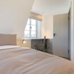 Schlafzimmer mit Bett, Schreibtisch und Fenster. Tür führt zu einem Ankleidezimmer.