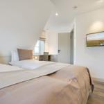 Schlafzimmer mit Doppelbett, Schreibtisch und Fernseher an der Wand.