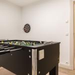 Fussballtisch mit Dartboard an der Wand. Treppenhaus im Hintergrund.