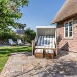 Haus mit Strohdach, Terrasse und Strandkorb im Garten.