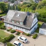 House with attic terrace, garden, and garage. Two white cars parked on the yard.