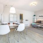 Living and dining area with gray sofa, white table set, and wooden floor.