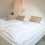 Bedroom with white bed, pillows, and towels. Wall lamps and wooden floor.