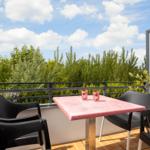 Terrace with table, chairs, and view of green trees under blue sky.